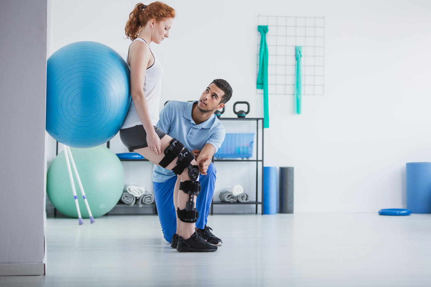 Eine Physiotherapeutin FH zeigt einem älteren Patienten die korrekte Ausführung einer Übung mit dem Theraband.