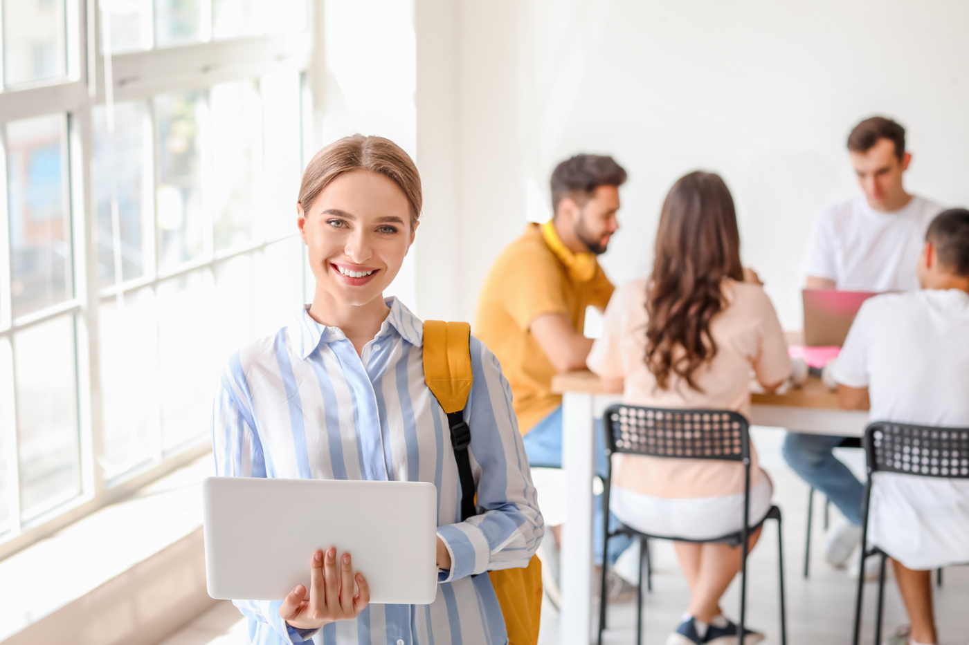 Schülerin einer Klasse zum Bürofachdiplom hält einen Laptop in der Hand und lächelt in die Kamera.
