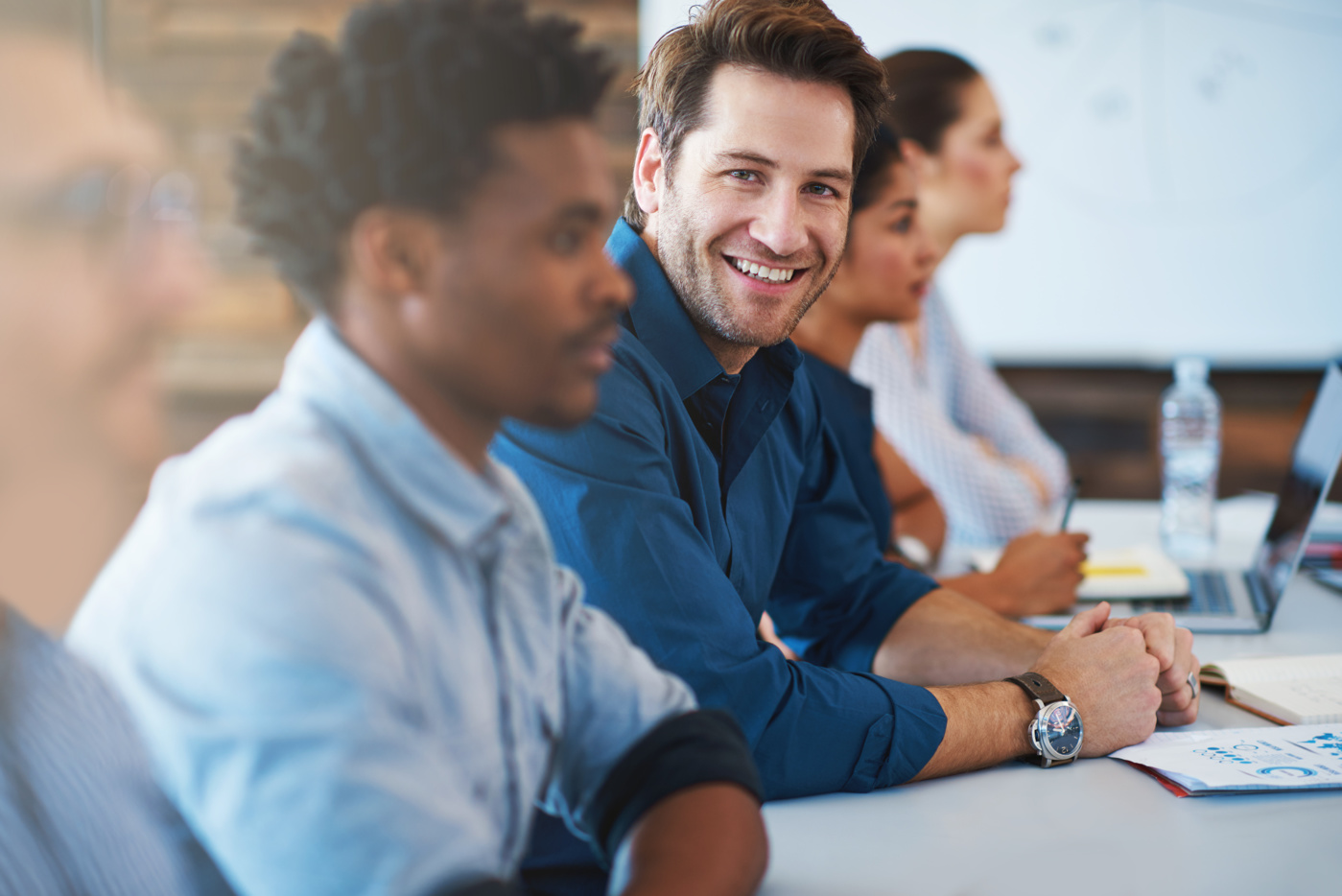 Absolvent eines Business Administration Studiums an einer FH sitzt mit anderen Arbeitskollegen/-innen in einer Management-Sitzung.