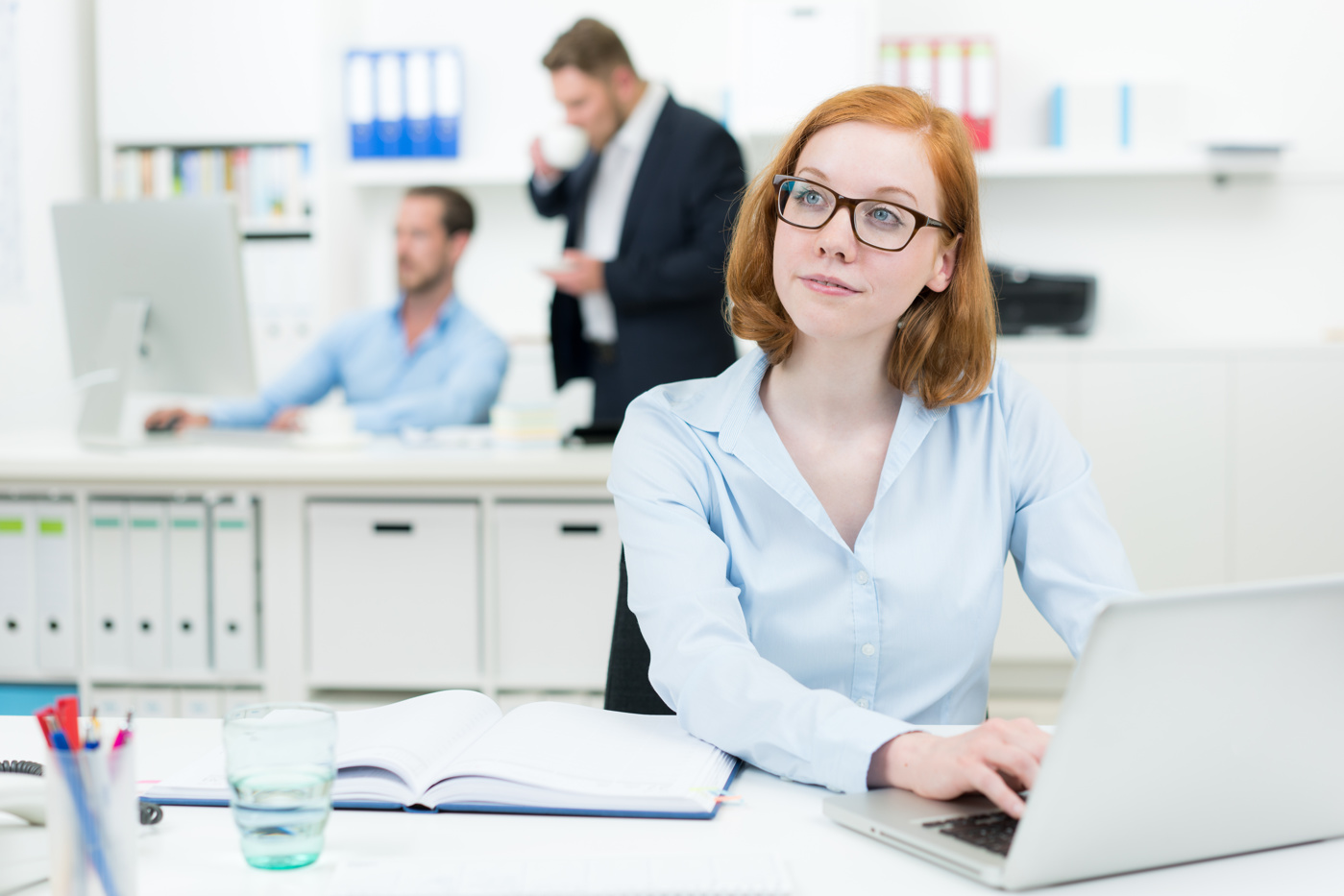 Eine Sachbearbeiterin Treuhand sitzt am Pult vor dem Laptopt und unterstützt ihren Vorgesetzten bei administrativen Arbeiten.