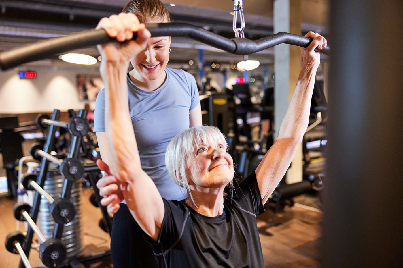 Eine Spezialistin Bewegungs- und Gesundheitsförderung mit eidg. Fachausweis leitet eine Kundin im Fitnessstudio an, ein Trainingsgerät korrekt zu benutzen.