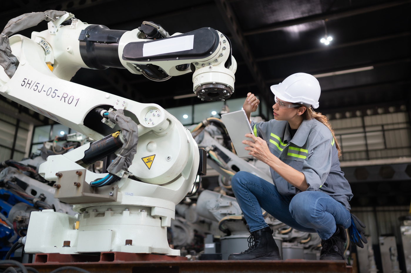 Eine Systemtechnikerin mit Abschluss an einer Fachhochschule kontrolliert einen Roboter der Industrie.