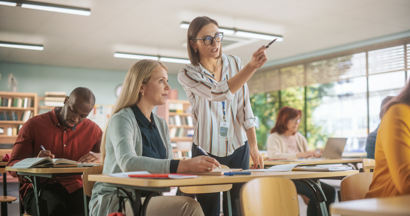 Eine Deutsch-Lehrerin geht auf eine individuelle Frage einer Teilnehmerin ein und zeigt mit dem Finger auf die Wandtafel.