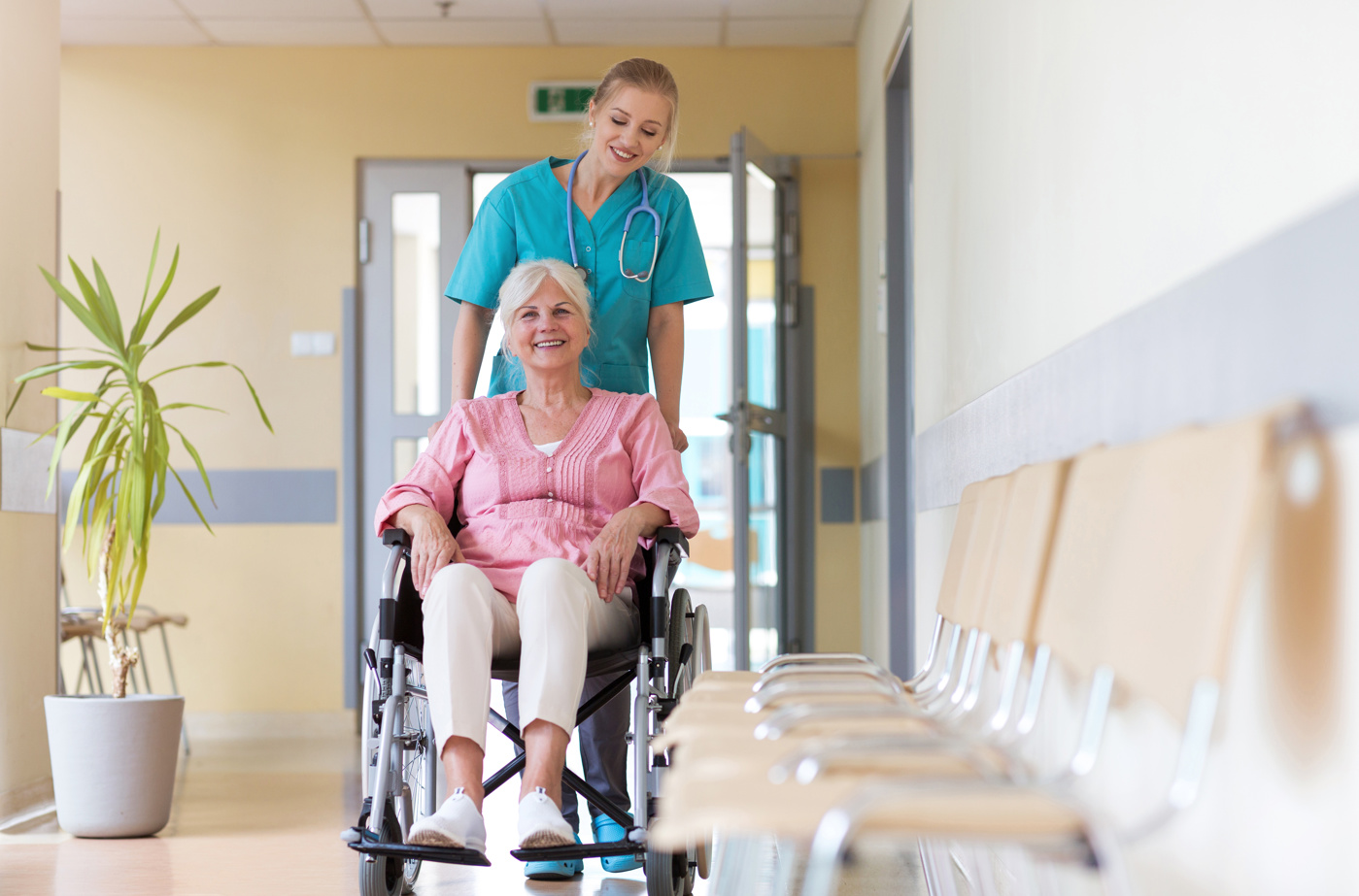 Eine Pflegerin schiebt eine Patientin im Rollstuhl den Gang im Krankenhaus entlang.