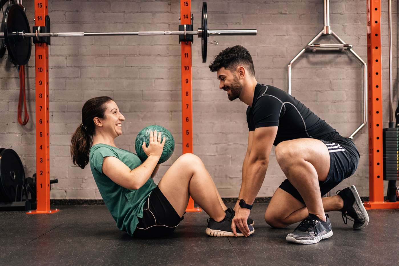 Ein Personaltrainer motiviert seine Kundin bei den Rumpfbeugen und überwacht deren korrekte Ausführung.